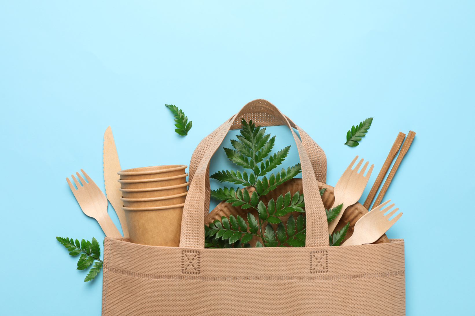 Eco bag with disposable tableware on blue background, space for